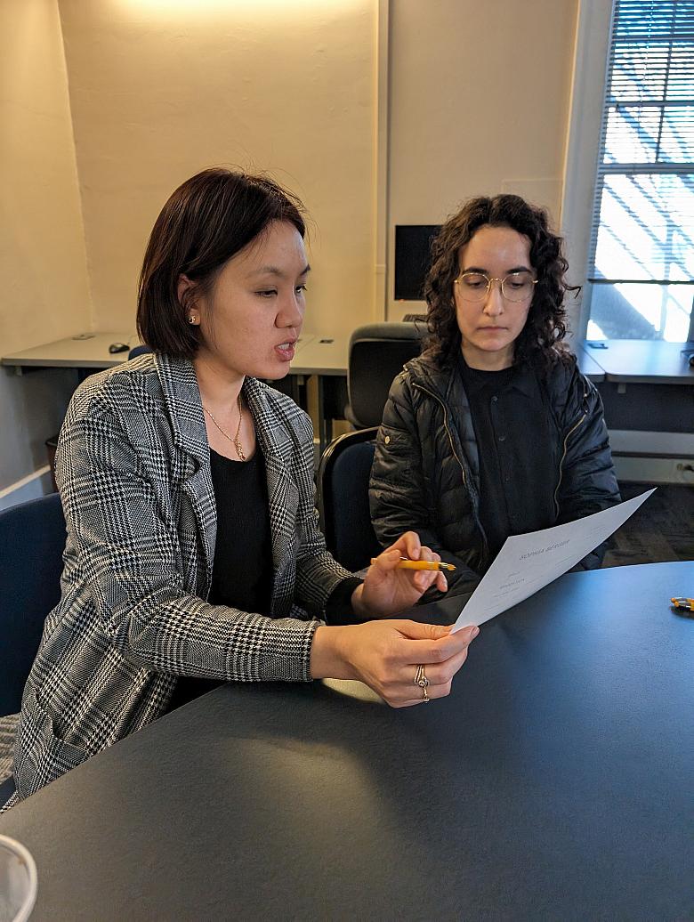 one person holds a piece of paper in their hand and the person next to her looks on